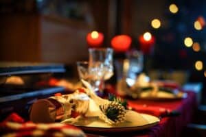 A photo of a Christmas table setting, with a red tablecloth, plates, glasses, pinecones, and a Christmas tree in the background in preparation for a West Texas Bariatric healthy holiday meal.